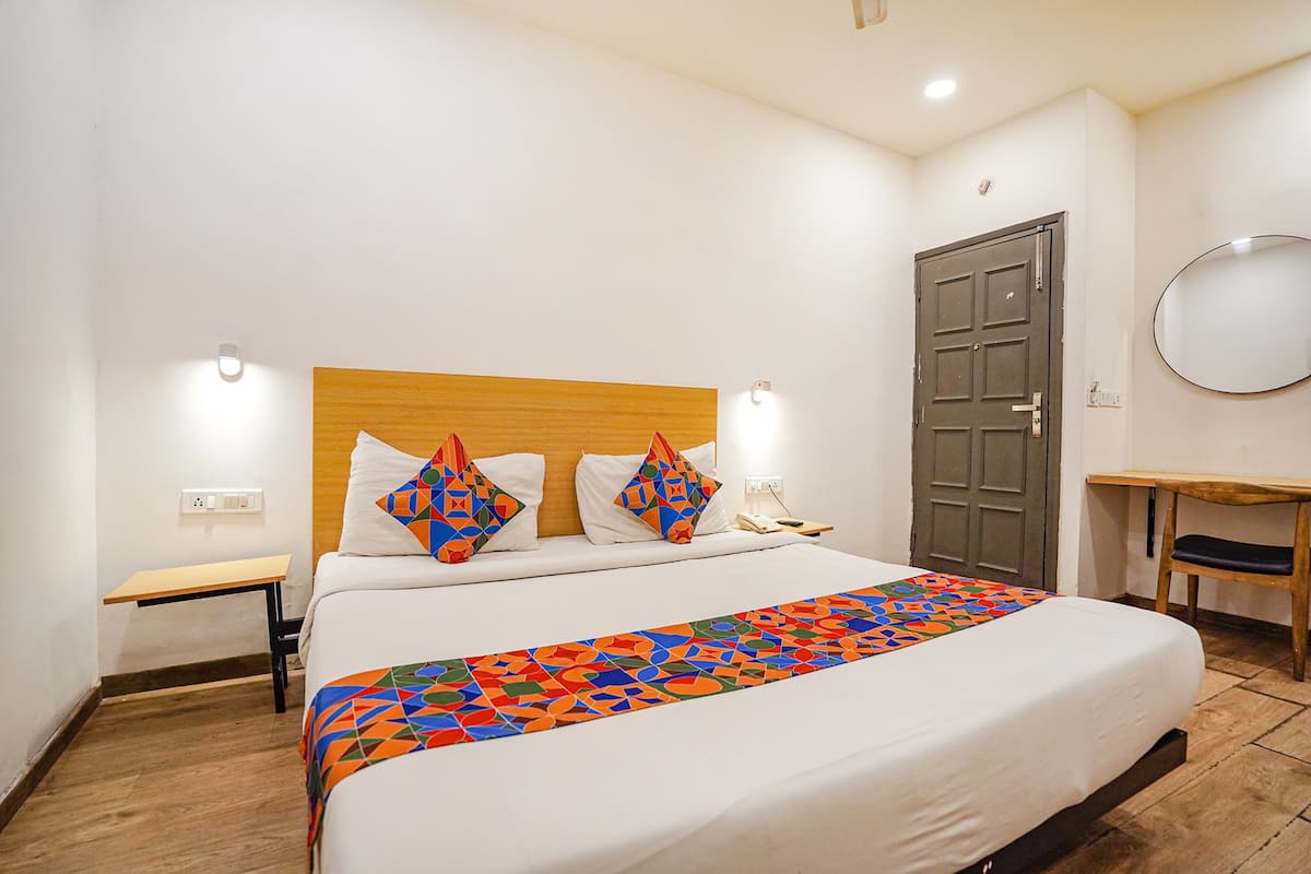 A hotel room with a bed, a wooden headboard, a nightstand, a desk, a mirror, and a door.