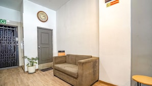 A lobby with a beige sofa, a clock, a 'No Smoking' sign, a potted plant, and a wooden floor.