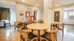 A dining area with round tables and chairs, a wooden floor, and framed pictures on the walls.