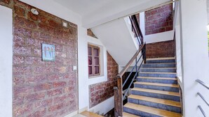 Una escalera de madera con barandales de metal, que conduce a un rellano con un muro de ladrillo y una ventana.