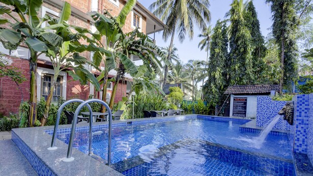 Una piscina con diseño de mosaicos azules, rodeada de exuberante vegetación y palmeras.