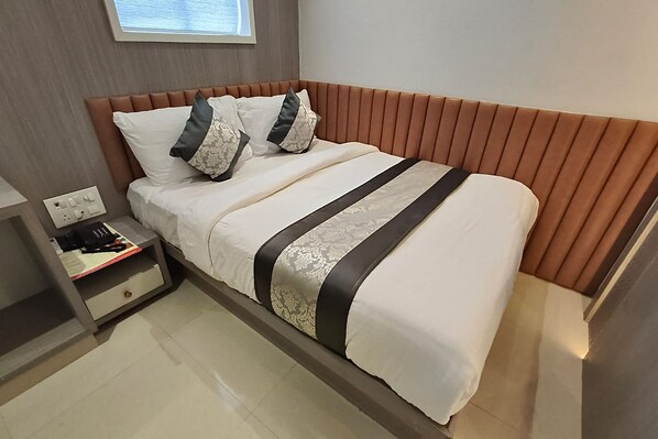 A neatly made bed with a striped bedspread and two pillows, a bedside table with a phone and a book, and a wall-mounted light fixture.