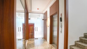 A hallway with a marble floor, wooden doors, and a phone on the wall. - Fabhotel Melody Boutique (Thane)