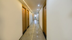 A long, narrow hallway with wooden doors on both sides, leading to a bright room at the end. - FabHotel Arjun Luxury Banquets and Rooms (New Delhi)