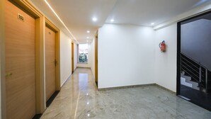 A hotel hallway with wooden doors numbered 103 and 102, a fire extinguisher on the wall, and a staircase leading to an upper floor. - FabHotel Arjun Luxury Banquets and Rooms (New Delhi)