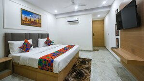 A modern bedroom with a bed, a ceiling fan, an air conditioning unit, a TV mounted on the wall, and a painting above the bed. - FabHotel Arjun Luxury Banquets and Rooms (New Delhi)