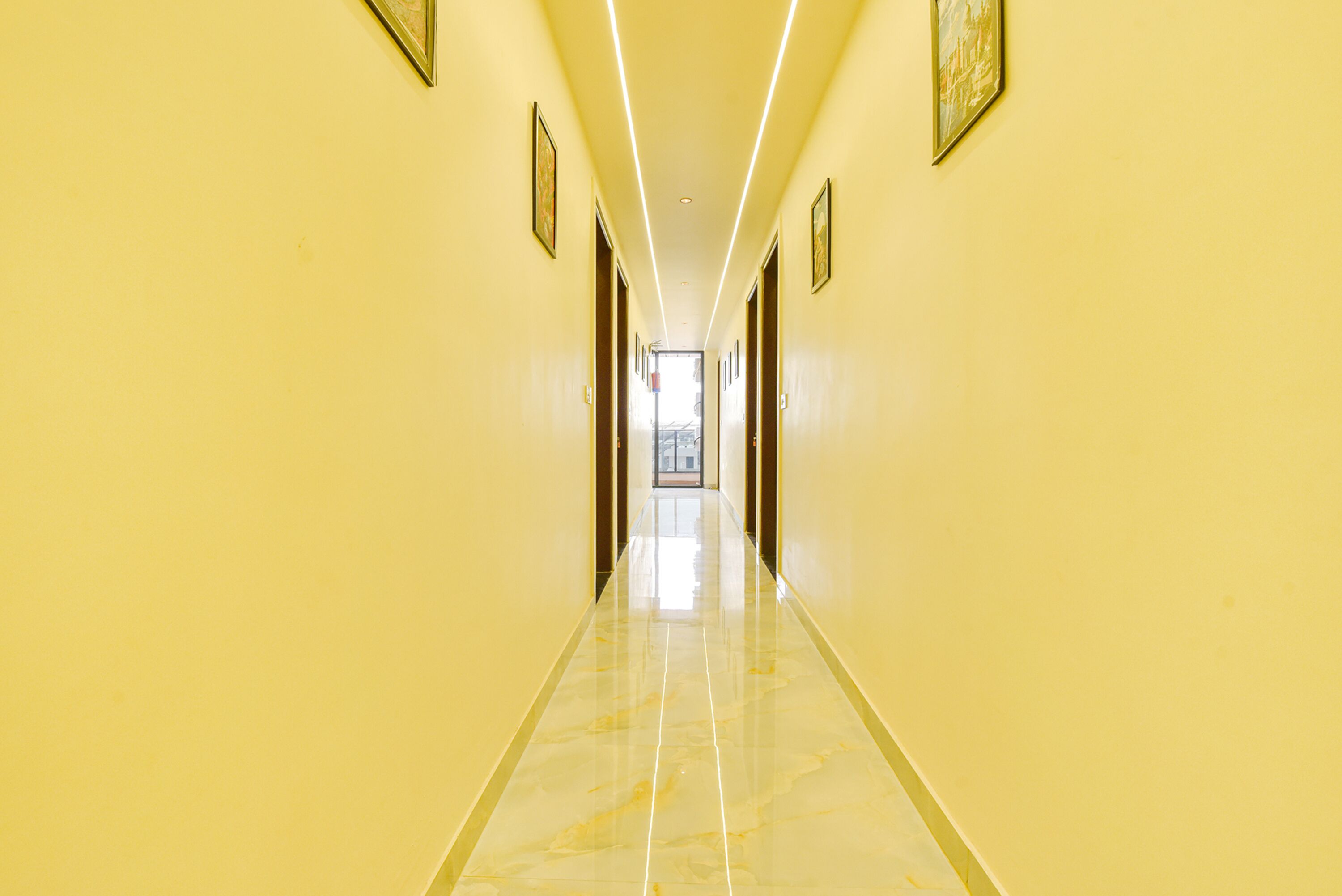 A long, narrow hallway with yellow walls and a shiny floor, leading to a bright room at the end.