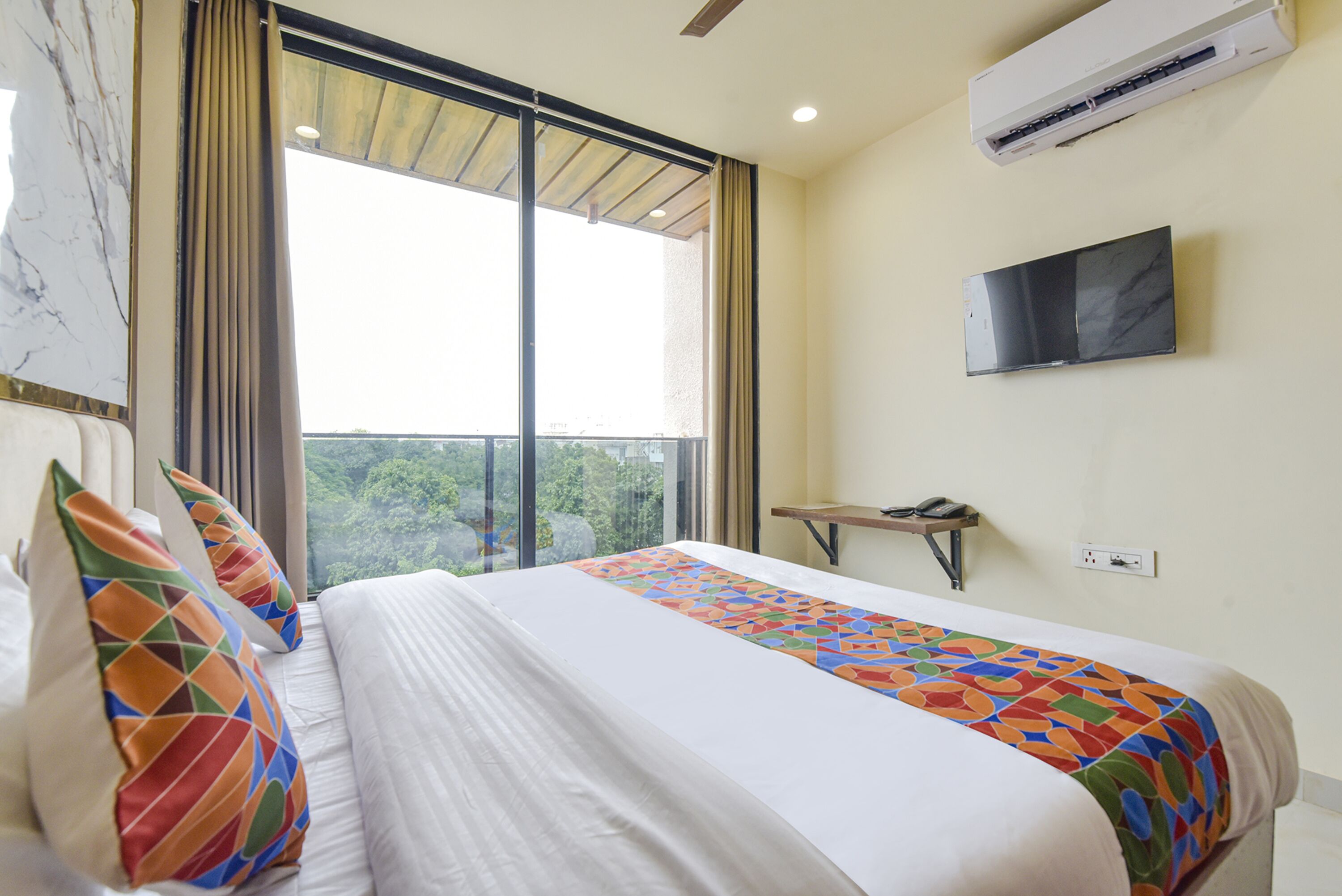 A hotel room with a large bed, a TV mounted on the wall, and a window with curtains.