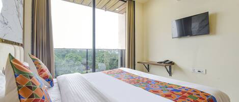 A hotel room with a large bed, a TV mounted on the wall, and a window with curtains.