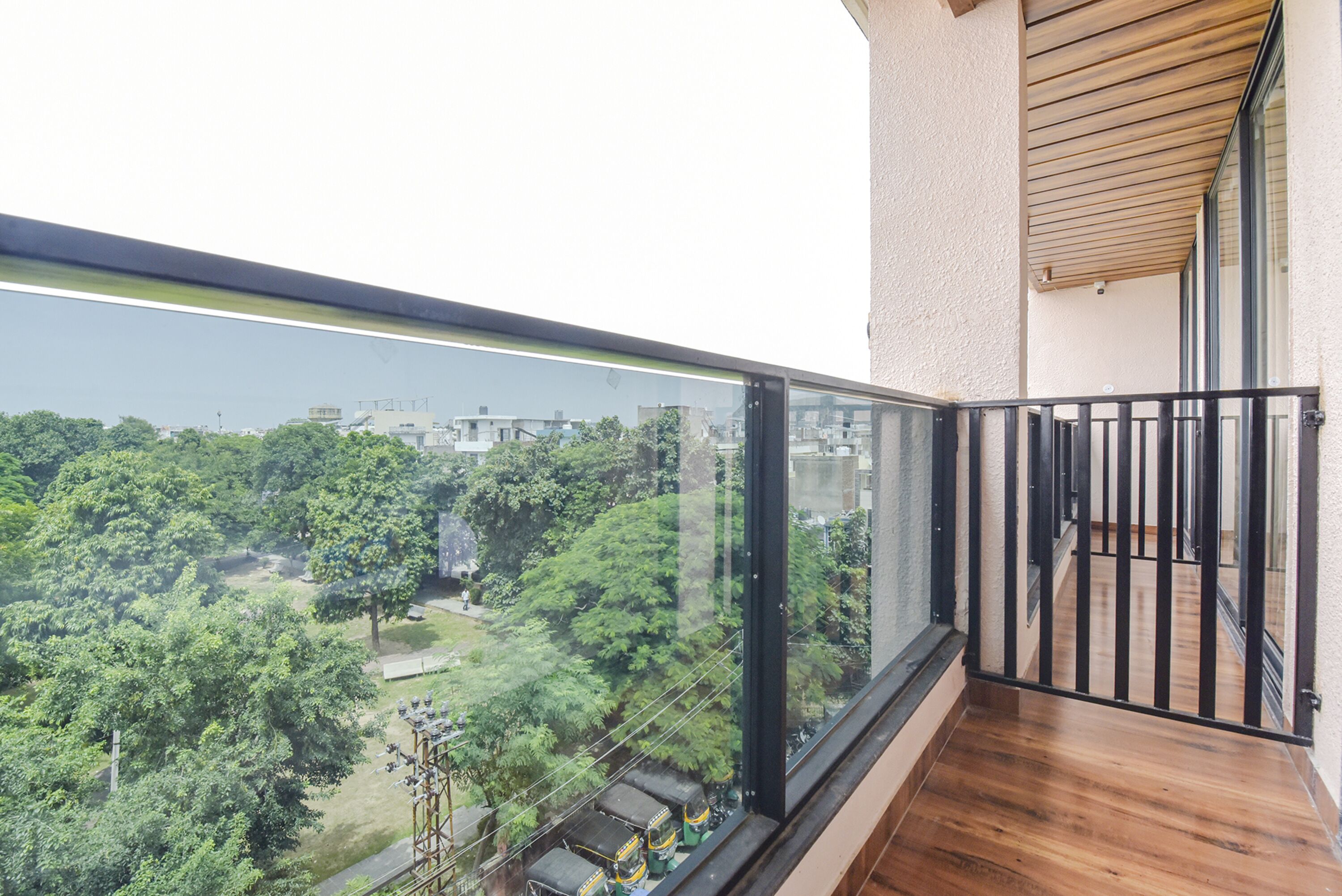 A balcony with a glass railing overlooking a park and buildings.