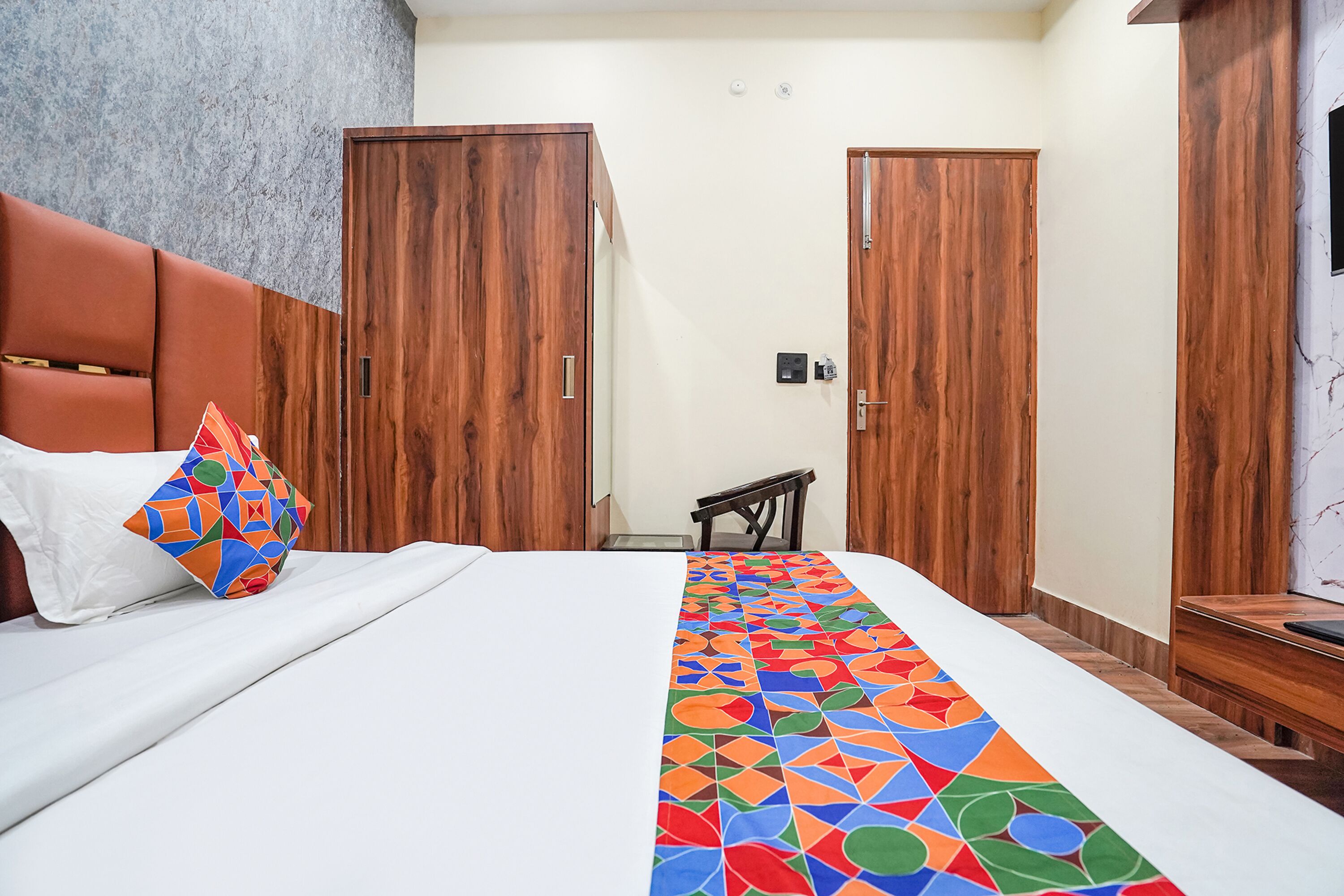 A hotel room with a bed, a wooden wardrobe, a small table, and a chair.