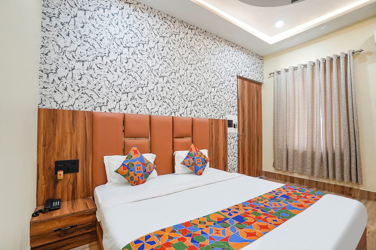 A hotel room with a bed, a wooden headboard, a nightstand with a phone, and a patterned wall.
