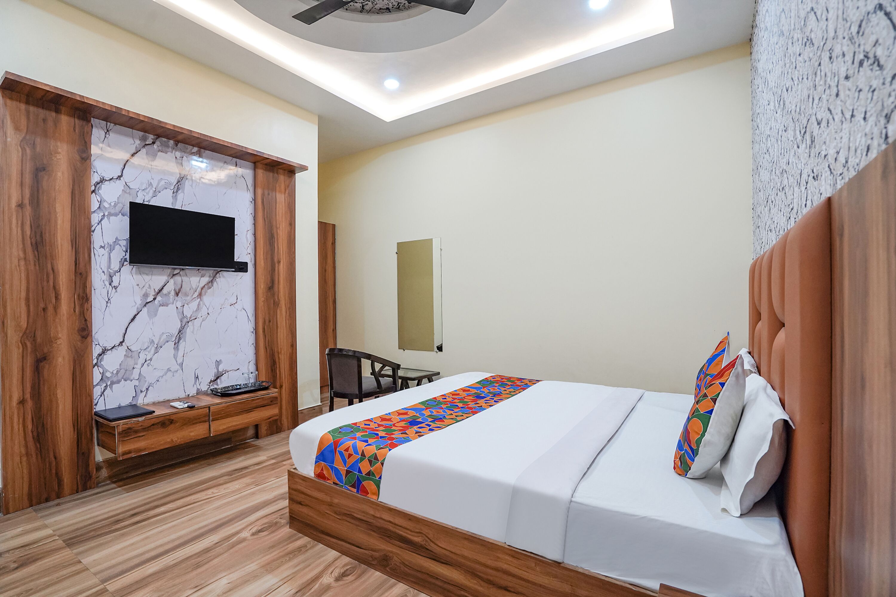 Een moderne hotelkamer met een houten bed, een aan een marmeren muur bevestigde televisie, een bureau en een stoel.