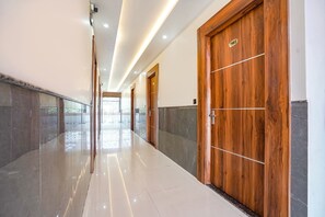 A hallway with polished floors, wooden doors, and a stone wall. - Fabhotel The Vrindavan Inn (Mathura)