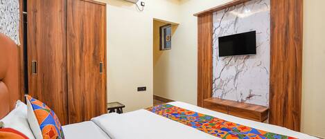 A bedroom with a bed, a TV mounted on a marble wall, wooden wardrobes, and an air conditioning unit.