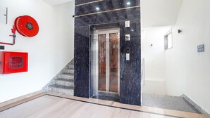 A modern elevator with a glass door, a red fire extinguisher, and a marble wall. - Fabhotel The Vrindavan Inn (Mathura)