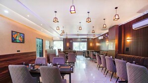 A modern restaurant with multiple dining tables and chairs, pendant lighting, and a large window providing natural light. - Fabhotel The Vrindavan Inn (Mathura)