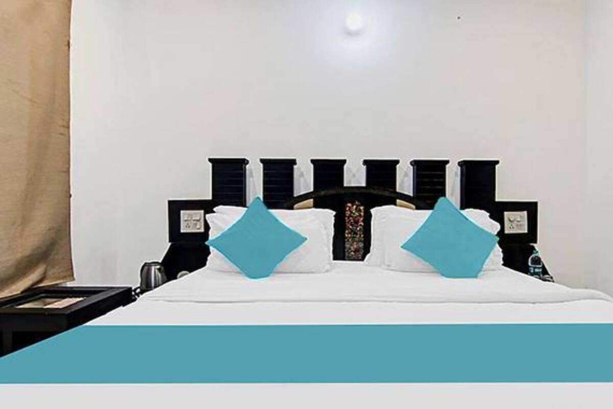 A neatly made bed with a white and teal bedspread, two teal pillows, and a black headboard with a decorative center.