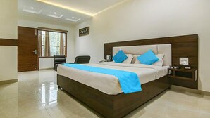 A large bed with a wooden headboard, a bedside table with a lamp, and a window with curtains. - Fabhotel Aditya And Kings (Panchkula)