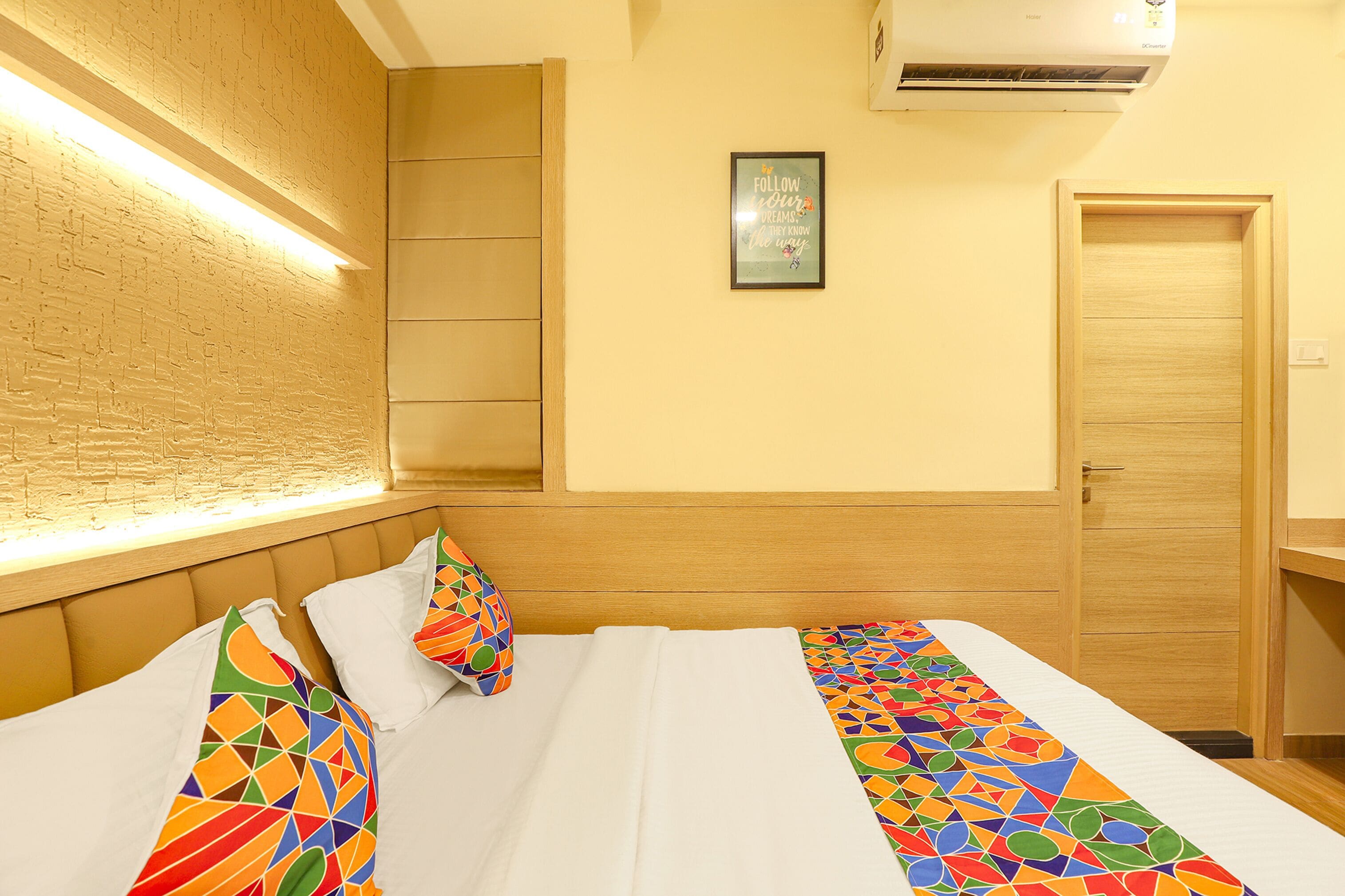 Une chambre d’hôtel avec un lit, une tête de lit, un climatiseur fixé au mur et une porte.