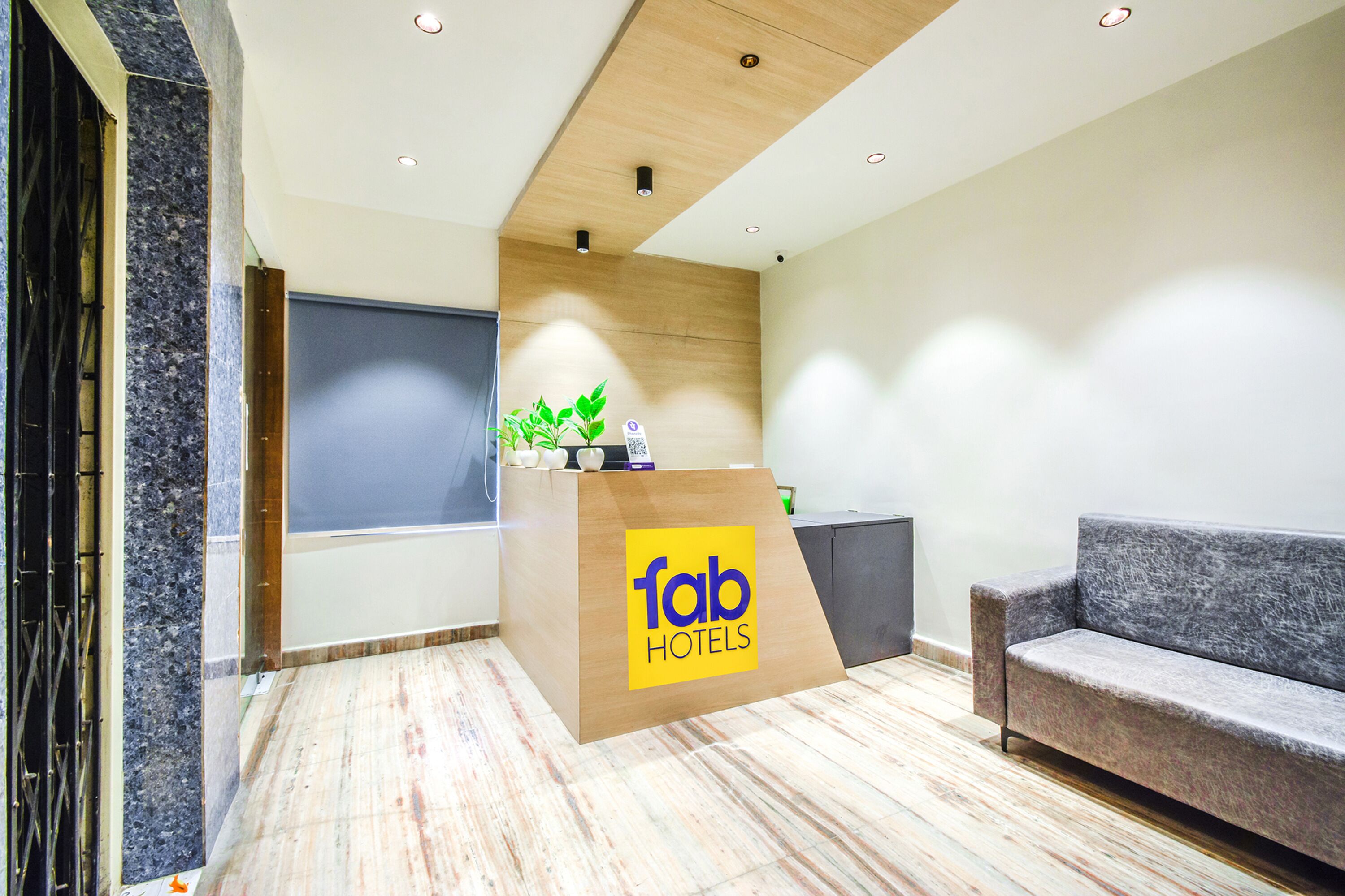A reception area with a wooden podium labeled "fab hotels," a grey sofa, and a marble floor.