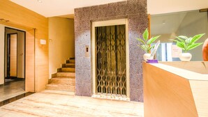Zona de recepción de un hotel con piso de mármol, un mostrador de recepción, una escalera y una puerta de seguridad.