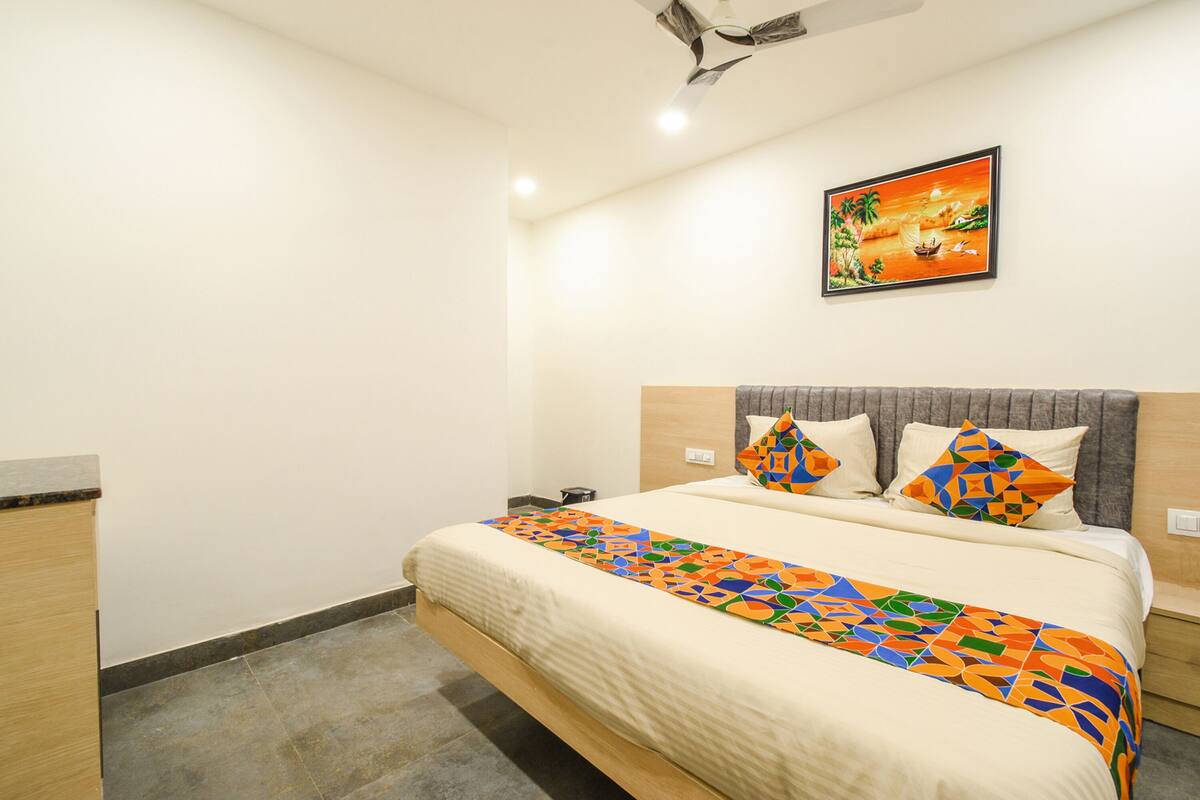 A hotel room with a bed, a nightstand, a painting on the wall, and a ceiling fan.