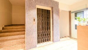 Una escalera conduce a una puerta con celosía metálica, un mostrador de recepción y una planta al fondo.