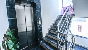 A modern elevator with a metallic finish, adjacent to a staircase with metal railings and dark steps. - Fabhotel The Grand Velvet (Noida)