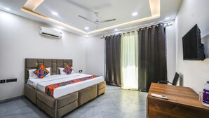 A modern hotel room with a bed, a desk, a ceiling fan, and a TV. - Fabhotel The Grand Velvet (Noida)