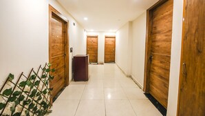 A hallway with wooden doors, a marble floor, and a plant. - Fabhotel The Grand Velvet (Noida)