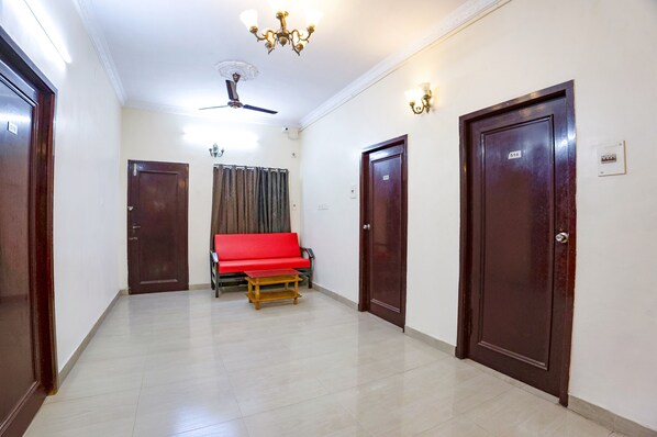 A hallway with a red sofa, wooden doors, and a ceiling fan. - Fabhotel Home Tree Service Apartment T Nagar (Chennai)