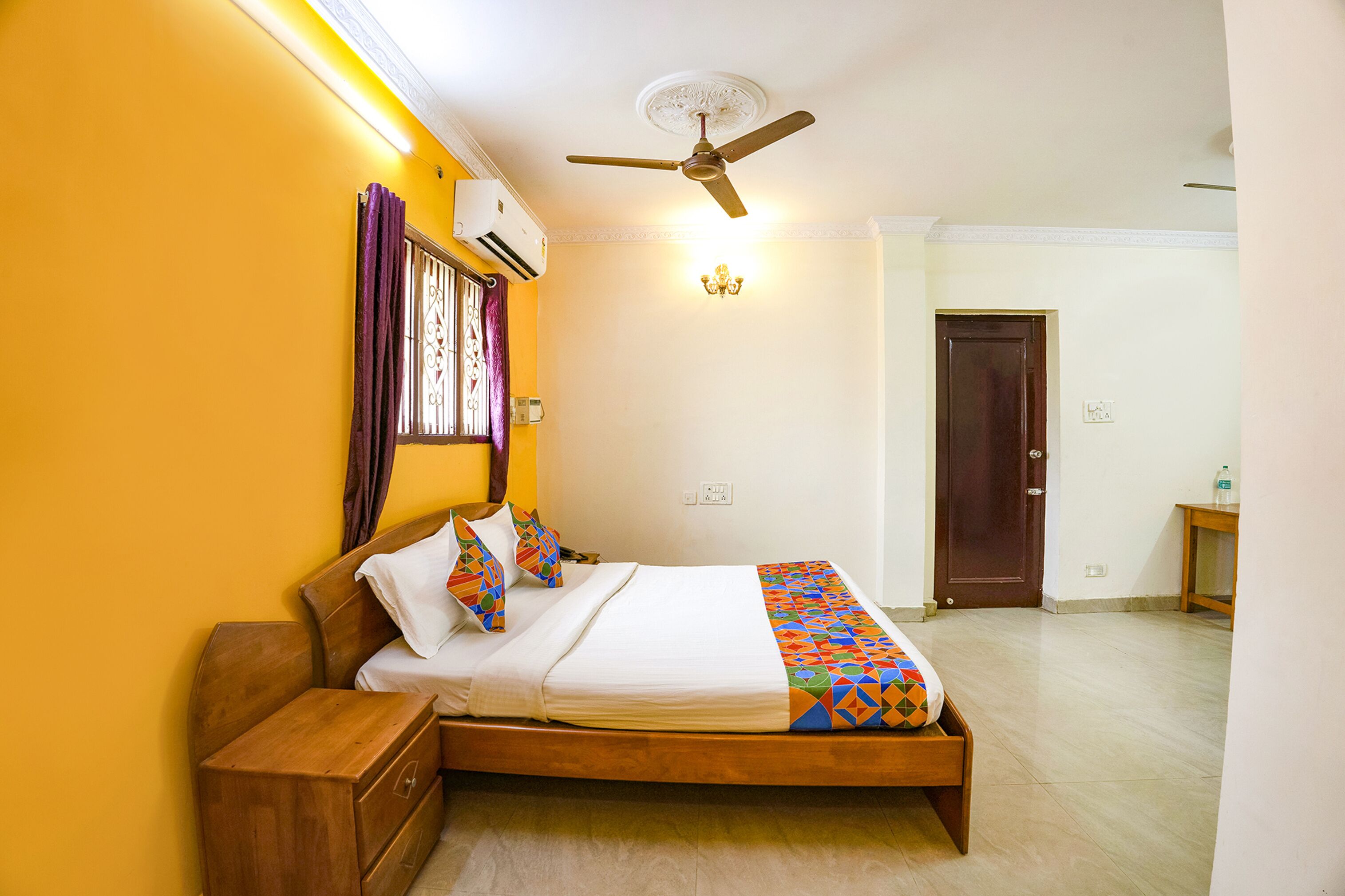 Une chambre avec un lit en bois, un ventilateur de plafond, un appareil de climatisation et une porte.