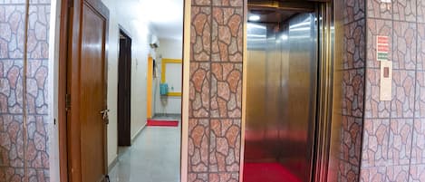 An elevator with a red carpet, a stone-patterned wall, and a door leading to a hallway with a red mat.