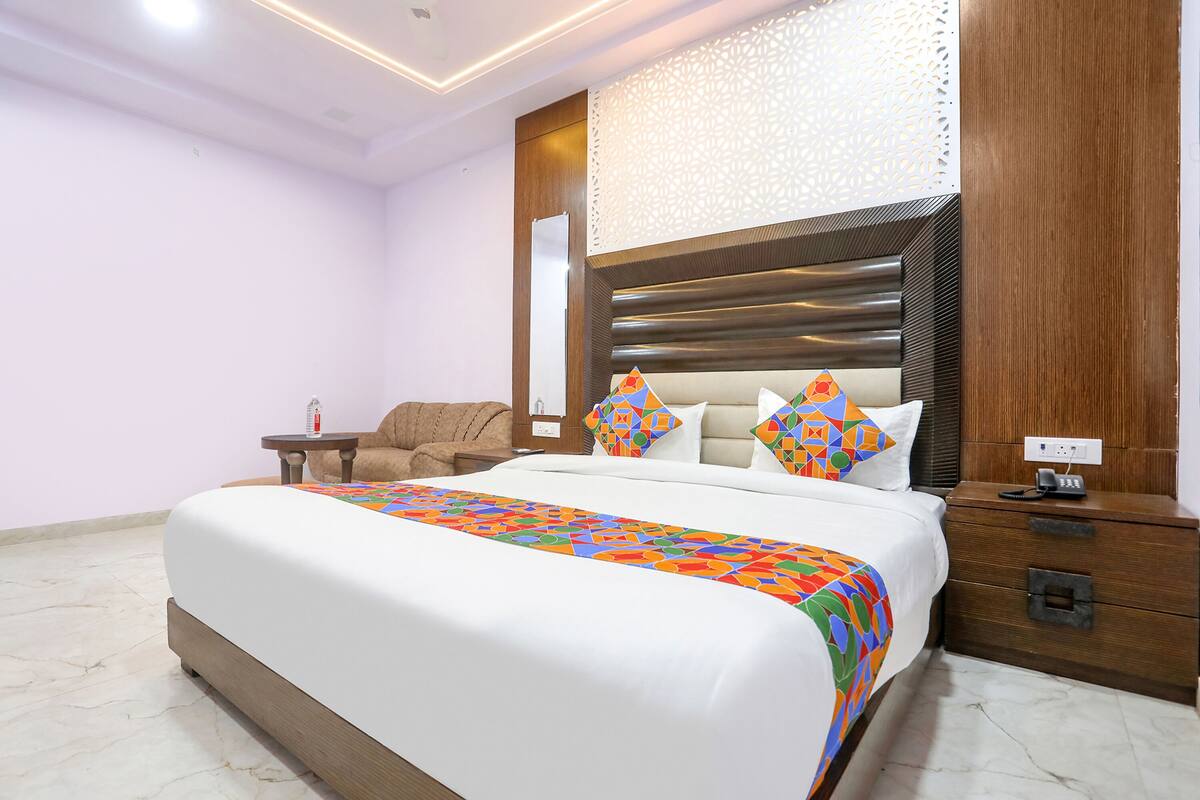A modern hotel room with a large bed, a wooden nightstand, a small table, and a decorative headboard.