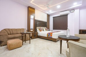 A modern hotel room with a sofa, a bed with a colorful blanket, a small table, and a ceiling fan. - Fabhotel Lords Valley (Kanpur)
