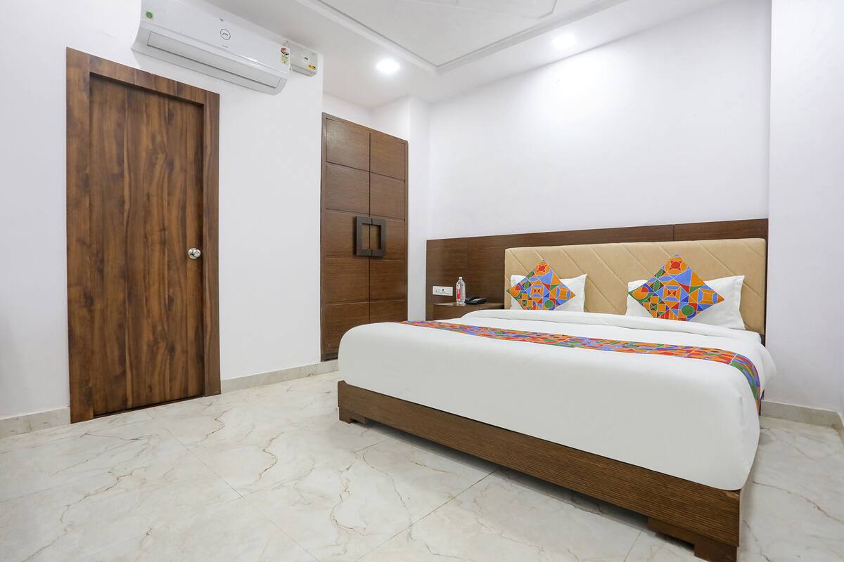 A hotel room with a wooden door, a bed with a beige headboard, and a patterned bedspread.