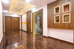A hallway with polished dark tiles, wooden doors, a staircase, and a wall with framed glass panels. - Fabhotel Lords Valley (Kanpur)