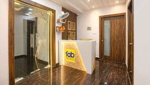 Ein Empfangsbereich mit modernem Design, inklusive einer Rezeption mit dem Schild 'fab hotels', einer Holztür und einem Wandventilator.