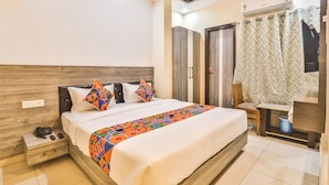 A hotel room with a bed, nightstand, wardrobe, and an air conditioning unit. - Fabhotel Ls Grand (Varanasi)