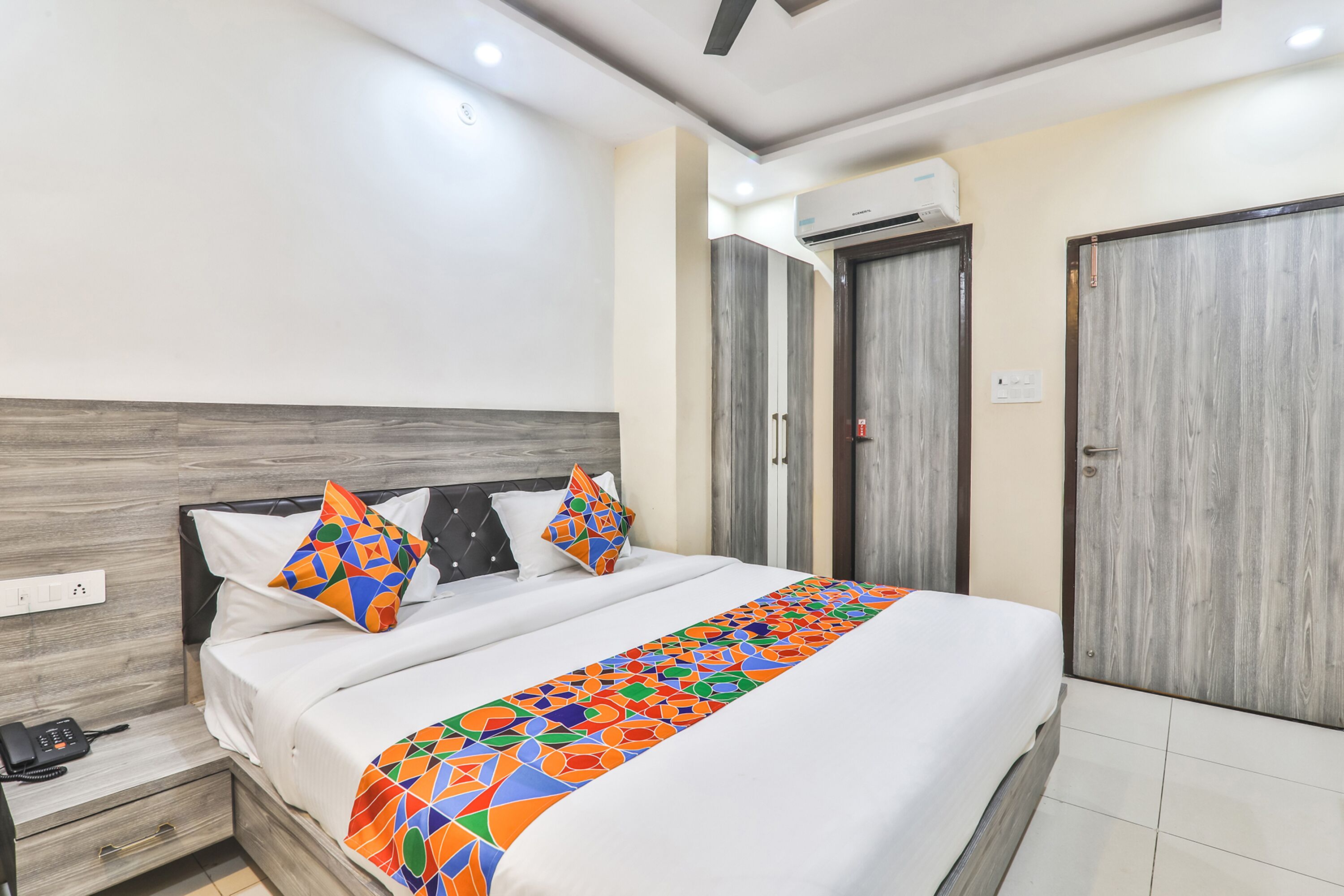 Una habitación de hotel con una cama, una mesita de noche con teléfono y un armario.