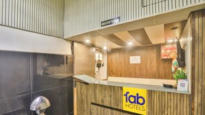A reception desk with a wooden finish, a reception sign, a digital screen, and a plant. - Fabhotel Ls Grand (Varanasi)