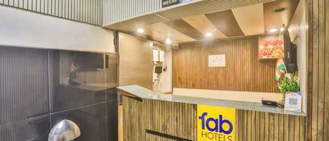 A reception desk with a wooden finish, a reception sign, a digital screen, and a plant.