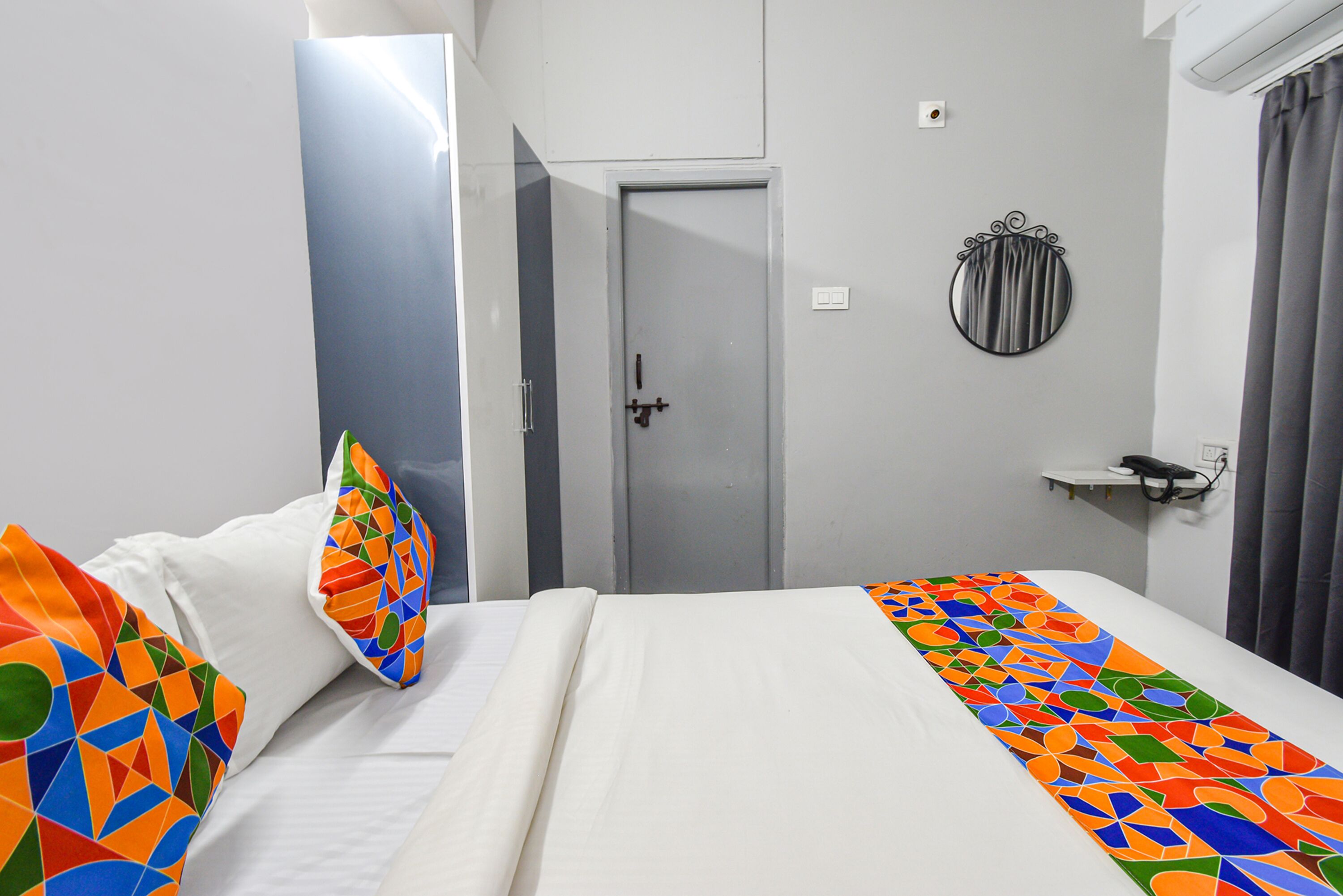 Une chambre d’hôtel avec un lit, une porte, un miroir et une petite étagère.