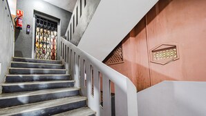 Een trap met een metalen hek aan de bovenkant, een brandblusser en een ventilatierooster op de muur.