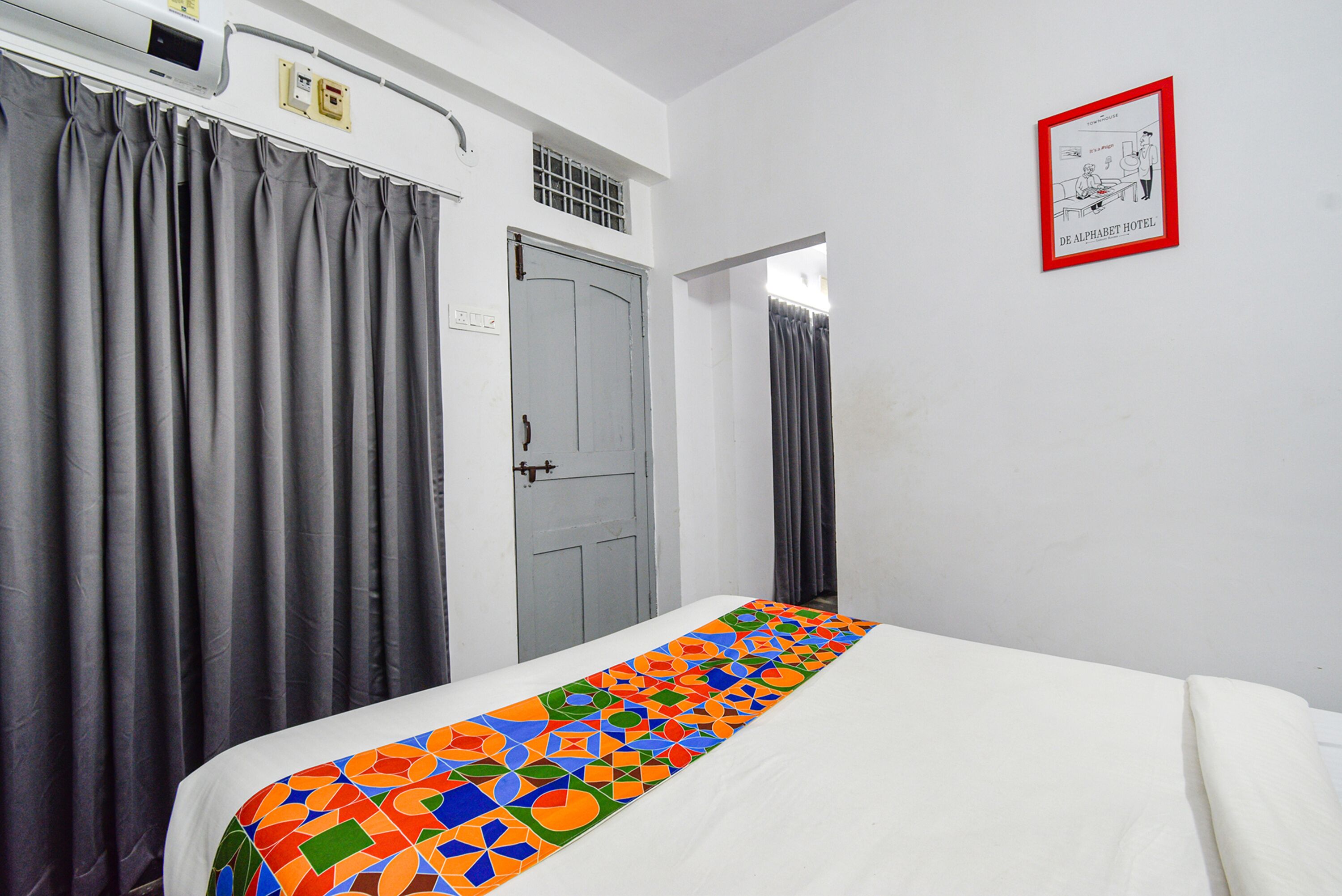 A hotel room with a bed, grey curtains, a white wall, and a framed picture.