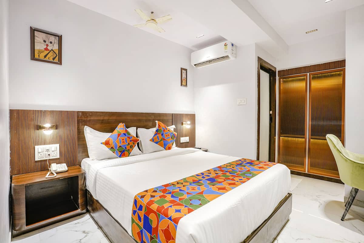 A hotel room with a large bed, a bedside table with a phone, a chair, a ceiling fan, and an air conditioning unit.