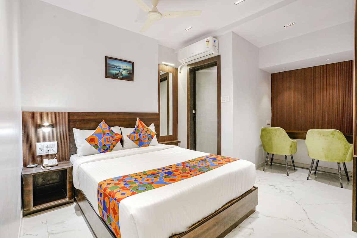 A hotel room with a bed, a desk, two chairs, a ceiling fan, and an air conditioning unit.