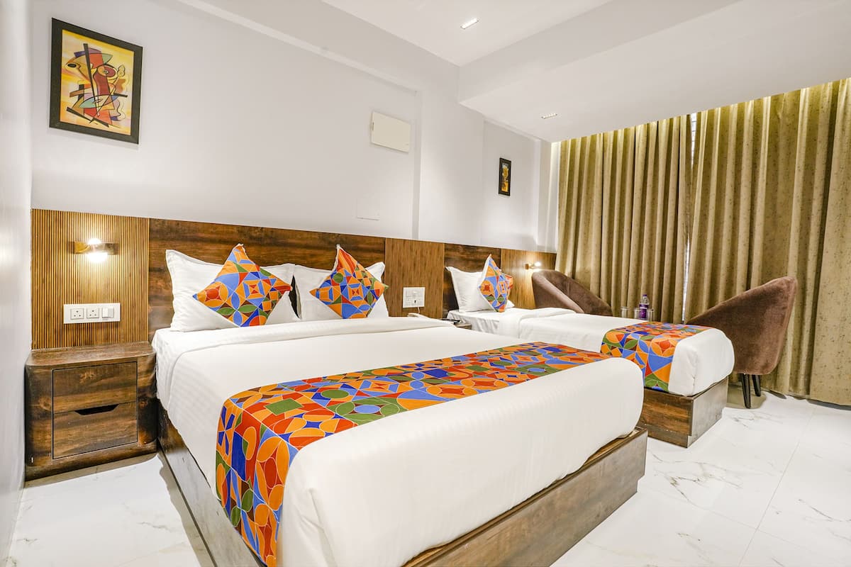 A hotel room with two beds, a wooden headboard, a large window with curtains, and a nightstand with a lamp.