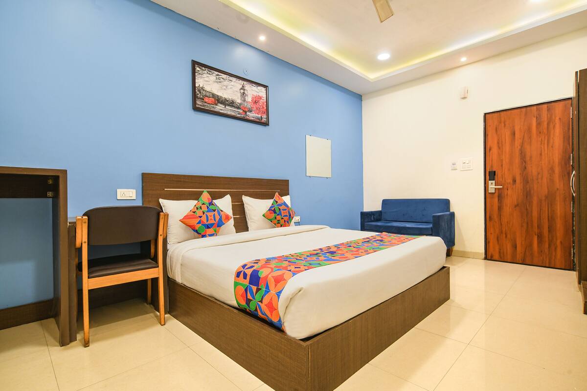 A hotel room with a bed, a chair, a desk, and a door.